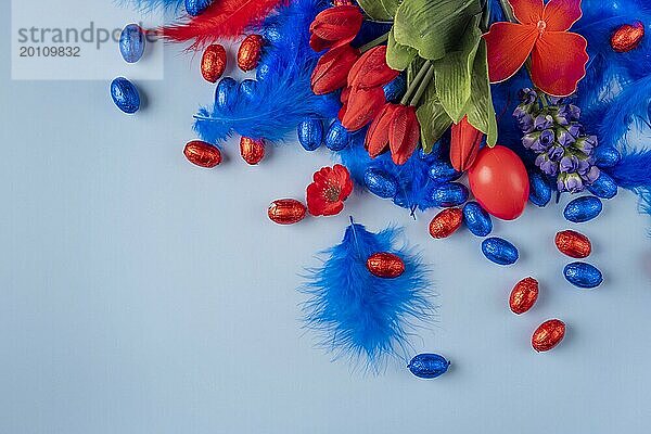 Fröhliche Osterdekoration mit einem roten Ei inmitten von Tulpen und Federn