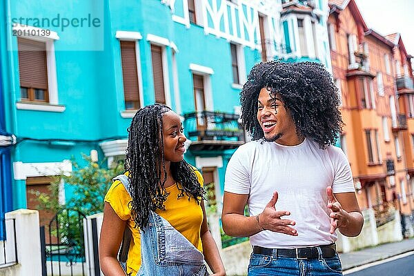 Zwei glückliche junge afrikanische Freunde unterhalten sich beim Besuch einer Straße mit bunten Häusern