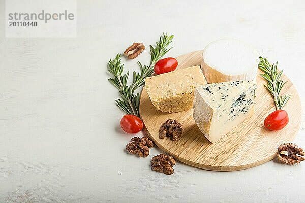 Blauschimmelkäse und verschiedene Käsesorten mit Rosmarin und Tomaten auf einem Holzbrett vor einem weißen Holzhintergrund. Seitenansicht  Kopierraum  selektiver Fokus