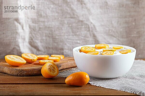 Griechischer Joghurt mit Kumquat Stücken in einem weißen Teller auf einem braunen Holzuntergrund  Nahaufnahme