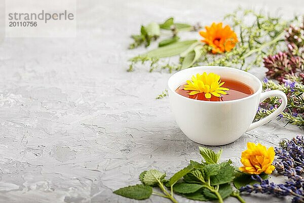 Tasse Kräutertee mit Ringelblume  Lavendel  Oregano  Ysop  Minze und Zitronenmelisse auf einem grauen Hintergrund aus Beton. Morninig  Frühling  gesundes Getränk Konzept. Seitenansicht  selektiver Fokus  Kopierraum