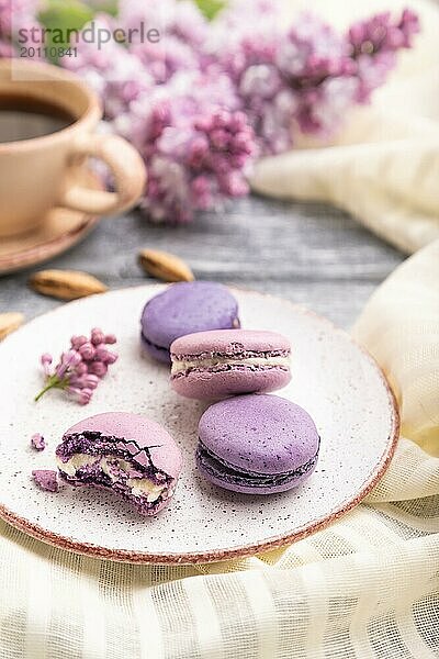 Lila Macarons oder Makronen Kuchen mit Tasse Kaffee auf einem grauen hölzernen Hintergrund und weißem Leinen Textil. Seitenansicht  Nahaufnahme  selektiver Fokus