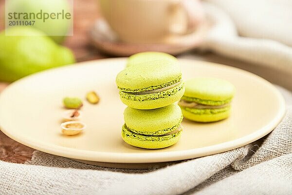 Grüne Macarons oder Makronen Kuchen mit Tasse Kaffee auf einem braunen Beton Hintergrund und Leinen Textil. Seitenansicht  Nahaufnahme  selektiver Fokus