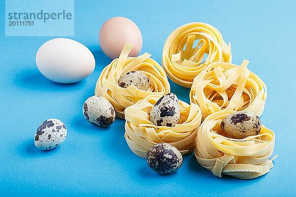 Rohe  ungekochte Tagliatelle Nudeln mit Wachteleiern auf blauem  pastellfarbenem Hintergrund. Seitenansicht  Nahaufnahme