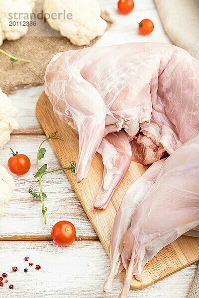 Ganzes rohes Kaninchen mit Blumenkohl  Tomaten und Gewürzen auf einem weißen Holzhintergrund und Leinenstoff. Seitenansicht  Nahaufnahme  selektiver Fokus