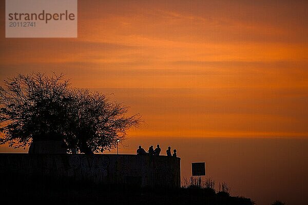 Silhouette einer Gruppe von Menschen sitzen auf einem Pier bei Sonnenuntergang