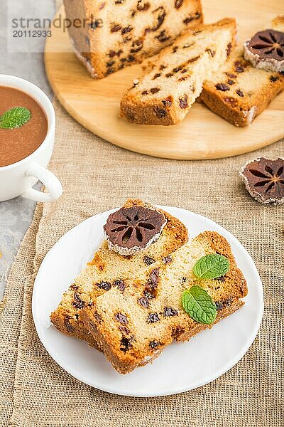 Hausgemachter Kuchen mit Rosinen  getrockneten Kaki und einer Tasse heißer Schokolade auf einem grauen Betonhintergrund und Leinenstoff. Seitenansicht  Nahaufnahme  selektiver Fokus