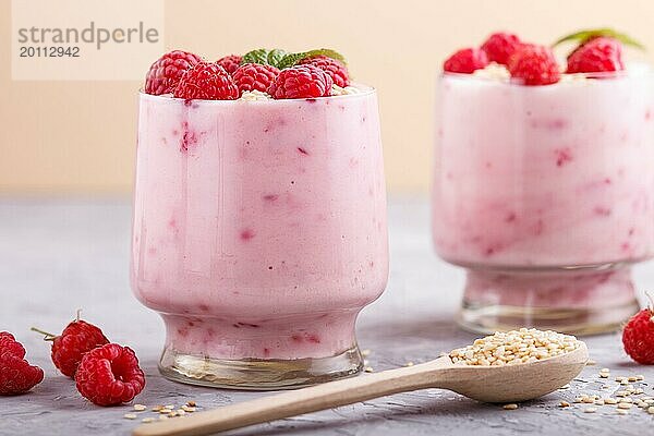 Joghurt mit Himbeere und Sesam in einem Glas und Holzlöffel auf grauem und orangem Hintergrund. Seitenansicht  Nahaufnahme