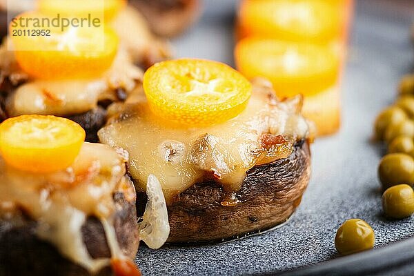 Gefüllte gebratene Champignons mit Käse  Kumquats und grünen Erbsen auf einem grauen Betonhintergrund. Keramikteller  Seitenansicht  Nahaufnahme  selektiver Fokus