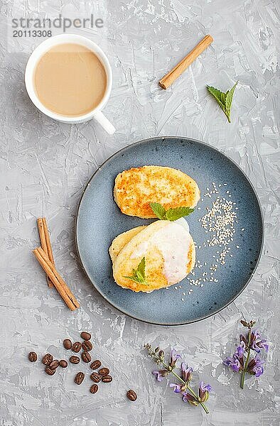 Käsepfannkuchen auf einem blauen Keramikteller und eine Tasse Kaffee auf einem grauen Betonhintergrund. Ansicht von oben  flach gelegt