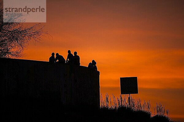 Silhouette einer Gruppe von Menschen sitzen auf einem Pier bei Sonnenuntergang