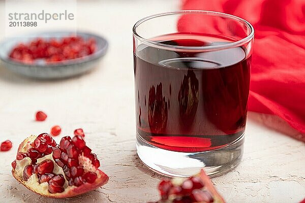 Glas Granatapfelsaft auf einem weißen Betonhintergrund mit rotem Stoff. Seitenansicht  Nahaufnahme  selektiver Fokus