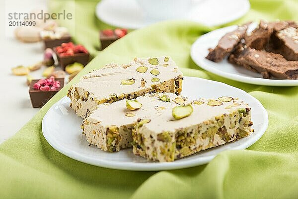 Traditionelle arabische Süßigkeiten Sesam Halva mit Schokolade und Pistazien und eine Tasse Kaffee auf grünem Textil Hintergrund. Seitenansicht  Nahaufnahme  selektiver Fokus