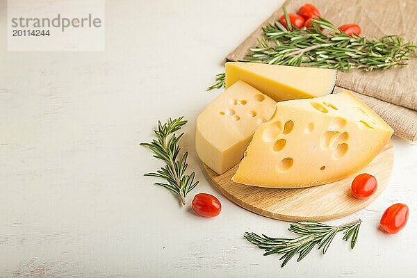 Verschiedene Käsesorten mit Rosmarin und Tomaten auf Holzbrett auf weißem Holzhintergrund und Leinentextil. Seitenansicht  Nahaufnahme  Kopierraum  selektiver Fokus