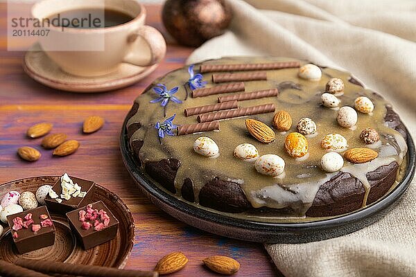 Hausgemachter Schokoladen Brownie Kuchen mit Karamellcreme und Mandeln mit einer Tasse Kaffee auf einem farbigen Holzhintergrund und Leinentuch. Seitenansicht  Nahaufnahme  selektiver Fokus