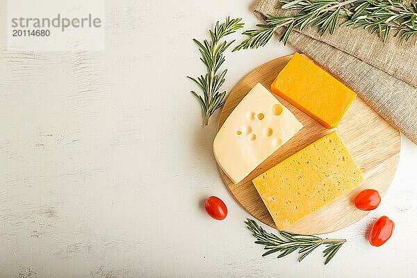 Verschiedene Käsesorten mit Rosmarin und Tomaten auf Holzbrett auf weißem Holzhintergrund und Leinenstoff. Draufsicht  Nahaufnahme  Kopiervorlage  Flat Lay