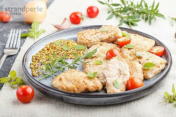 Gebratene Schweinekoteletts mit Tomaten und Kräutern auf einem grauen Keramikteller auf schwarzem Betonhintergrund und Leinentuch. Seitenansicht  Nahaufnahme  selektiver Fokus