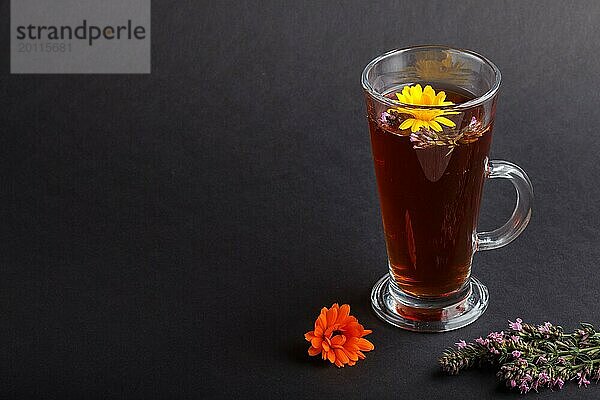 Glas Kräutertee mit Ringelblume und Ysop auf einem schwarzen Hintergrund. Morgens  Frühling  gesundes Getränk Konzept. Seitenansicht  Kopie Raum