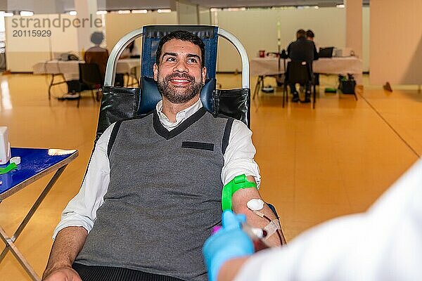 Altruistisch lächelnder Mann sitzt auf einem bequemen Stuhl  während er in einem Pavillon Blut spendet