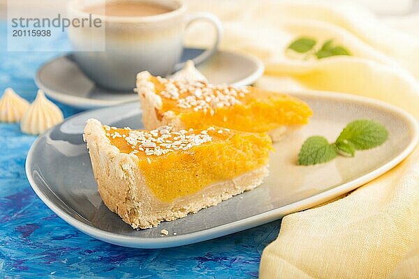 Zwei Stücke traditioneller amerikanischer Kürbiskuchen mit einer Tasse Kaffee auf einem blauen Betonhintergrund und gelbem Textil. Seitenansicht  Nahaufnahme  Kontrast  selektiver Fokus