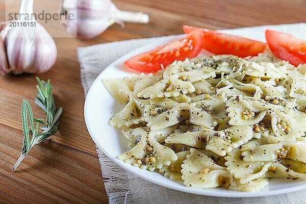 Farfalle Nudeln mit Pesto Soße  Tomaten und Käse auf einer Leinentischdecke auf einem braunen Holzhintergrund. Nahaufnahme  selektiver Fokus