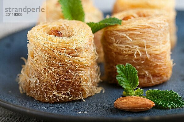 Kunafa  traditionelle arabische Süßigkeiten in blauem Keramikteller auf grauem Betonhintergrund. Seitenansicht  Nahaufnahme  selektiver Fokus