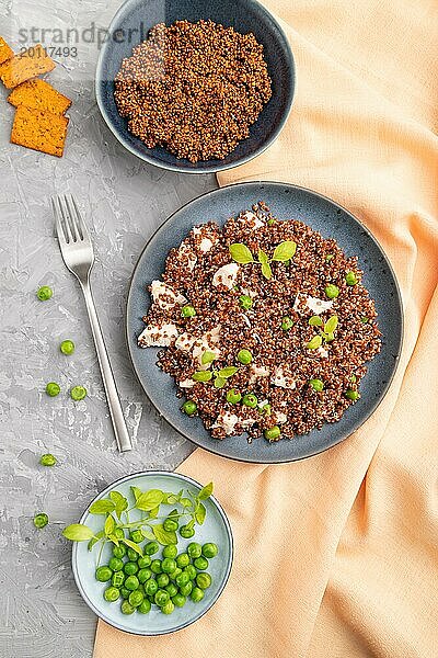 Quinoa Brei mit grüner Erbse und Huhn auf Keramikteller auf grauem Betonhintergrund und orangefarbenem Textil. Draufsicht  flach gelegt  Nahaufnahme