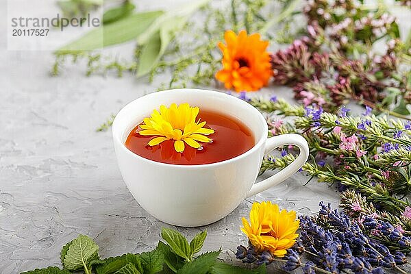 Tasse Kräutertee mit Ringelblume  Lavendel  Oregano  Ysop  Minze und Zitronenmelisse auf einem grauen Hintergrund aus Beton. Morninig  Frühling  gesundes Getränk Konzept. Seitenansicht  selektiver Fokus