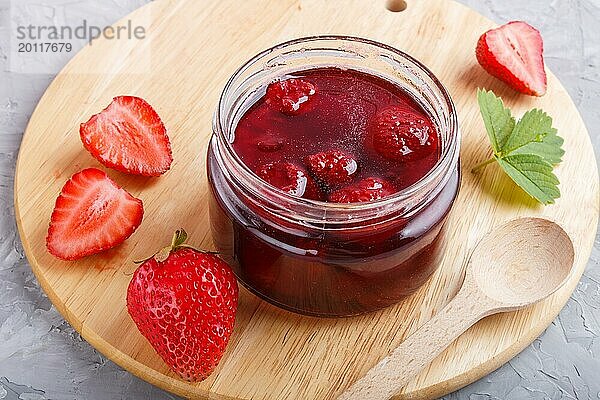 Erdbeermarmelade in einem Glas mit Beeren und Blättern auf grauem Betonhintergrund. Hausgemacht  Nahaufnahme  Seitenansicht  selektiver Fokus