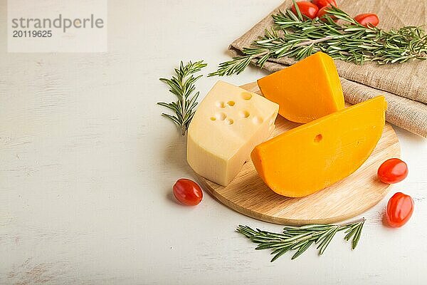 Verschiedene Käsesorten mit Rosmarin und Tomaten auf Holzbrett auf weißem Holzhintergrund und Leinentextil. Seitenansicht  Nahaufnahme  Kopierraum  selektiver Fokus