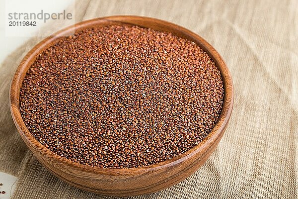 Holzschale mit rohen roten Quinoa Samen auf weißem Holzhintergrund und Leinenstoff. Seitenansicht  Nahaufnahme  selektiver Fokus