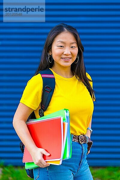 Vertikales Foto eines chinesischen Studenten  der Lehrbücher hält und in die Kamera lächelt