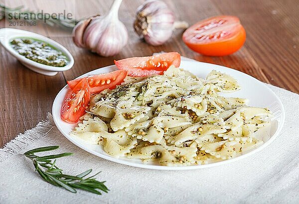 Farfalle Nudeln mit Pesto Soße  Tomaten und Käse auf einer Leinentischdecke auf einem braunen Holzhintergrund. Nahaufnahme  selektiver Fokus