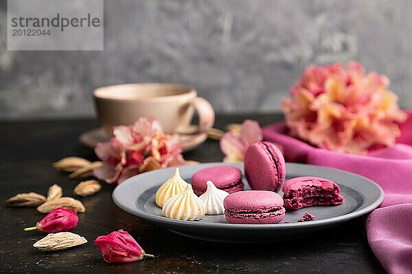 Lila Makronen oder Makronen Kuchen mit Tasse Kaffee auf einem schwarzen Beton Hintergrund und rosa Textil. Seitenansicht  Nahaufnahme  selektiver Fokus