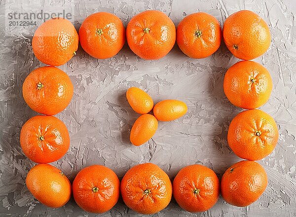 Reihen von Mandarinen  die ein Rechteck bilden  und drei Kumquats im Inneren auf einem grauen Betonhintergrund  Draufsicht  flach gelegt