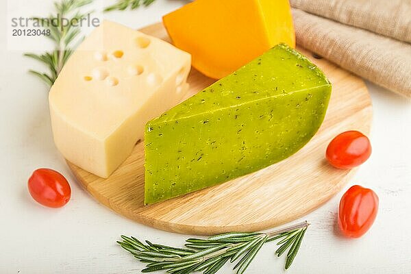 Grüner Basilikumkäse und verschiedene Käsesorten mit Rosmarin und Tomaten auf einem Holzbrett auf einem weißen Holzhintergrund. Seitenansicht  Nahaufnahme  selektiver Fokus