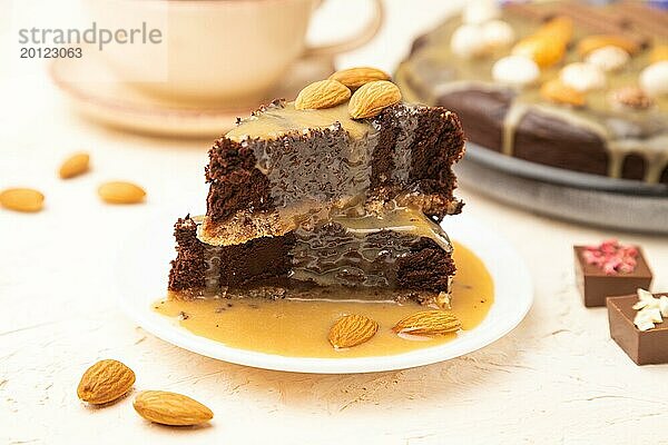 Stücke von Schokoladen Brownie Kuchen mit Karamellcreme und Mandeln auf einem weißen Betonhintergrund. Seitenansicht  Nahaufnahme  selektiver Fokus