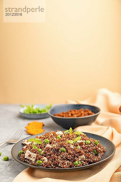 Quinoa Brei mit grüner Erbse und Huhn auf Keramikteller auf grauem Betonhintergrund und orangefarbenem Textil. Seitenansicht  Kopierraum  selektiver Fokus