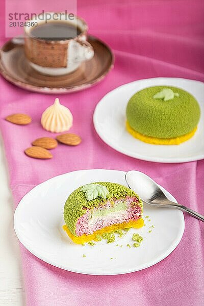 Grüner Mousse Kuchen mit Pistazien und Erdbeersahne auf weißem Holzhintergrund und rosa Stoff. Seitenansicht  Nahaufnahme  selektiver Fokus