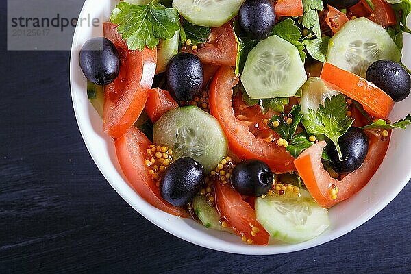 Vegetarischer Salat aus Tomaten  Gurken  Petersilie  Oliven und Senf auf schwarzem Holzuntergrund  Nahaufnahme  selektiver Fokus