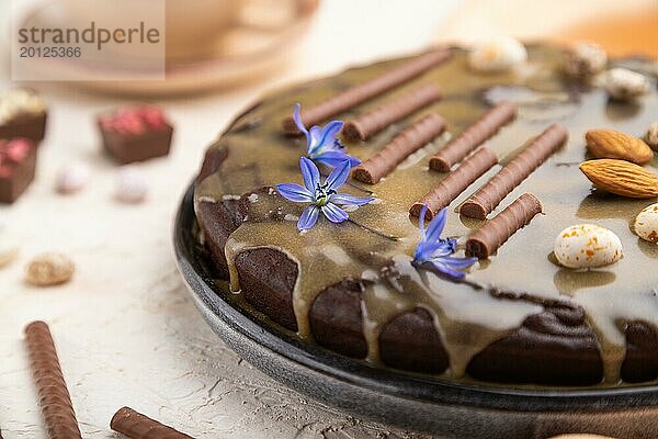 Hausgemachter Schokoladen Brownie Kuchen mit Karamellcreme und Mandeln mit einer Tasse Kaffee auf einem weißen Betonhintergrund und orangefarbenem Textil. Seitenansicht  Nahaufnahme  selektiver Fokus