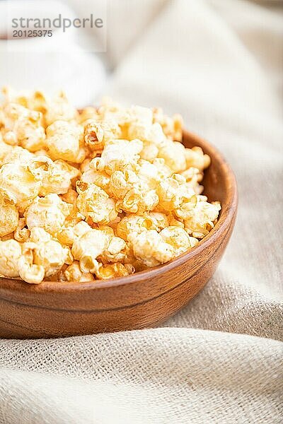 Popcorn mit Karamell in einer Holzschüssel und eine Tasse Kaffee auf einem weißen Holzhintergrund und Leinenstoff. Seitenansicht  Nahaufnahme  selektiver Fokus