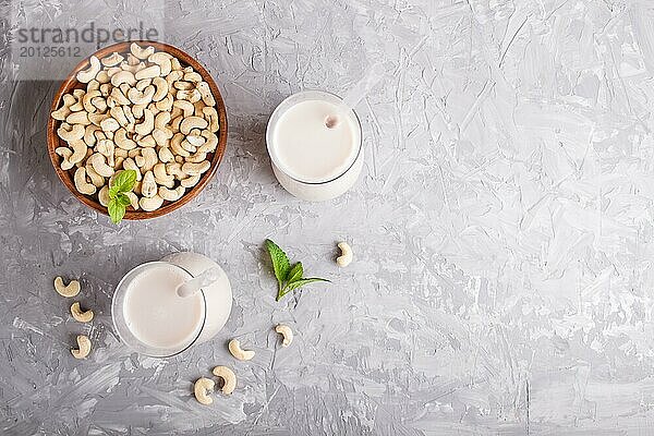 Biologische milchfreie Cashew Milch im Glas und Holzteller mit Cashew Nüssen auf grauem Beton Hintergrund. Vegane gesunde Ernährung Konzept  flach legen  Draufsicht  Kopie Raum