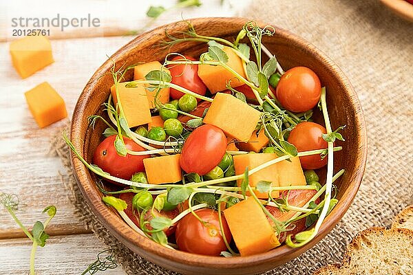 Vegetarischer Gemüsesalat aus Tomaten  Kürbis  mikrogrünen Erbsensprossen auf weißem Holzhintergrund und Leinentuch. Seitenansicht  Nahaufnahme  selektiver Fokus