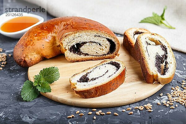 Hausgemachte Hefebrötchen mit Mohn und Honig auf einem hölzernen Küchenbrett auf einem schwarzen Betonhintergrund. Seitenansicht. Nahaufnahme  selektiver Fokus