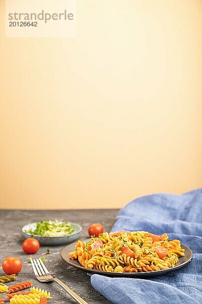 Tortiglioni Grießnudeln mit Tomaten und Mikrogrünsprossen auf schwarzem und orangefarbenem Hintergrund und blauem Textil. Seitenansicht  Kopierraum  selektiver Fokus