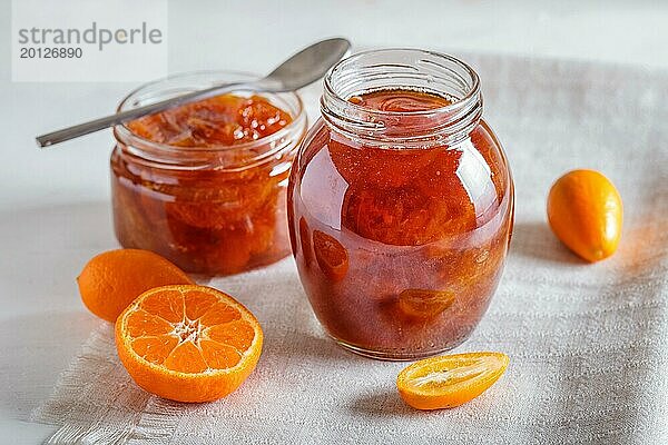 Mandarinen und Kumquatmarmelade in einem Glas mit frischen Früchten auf weißem Hintergrund. Hausgemacht  Nahaufnahme