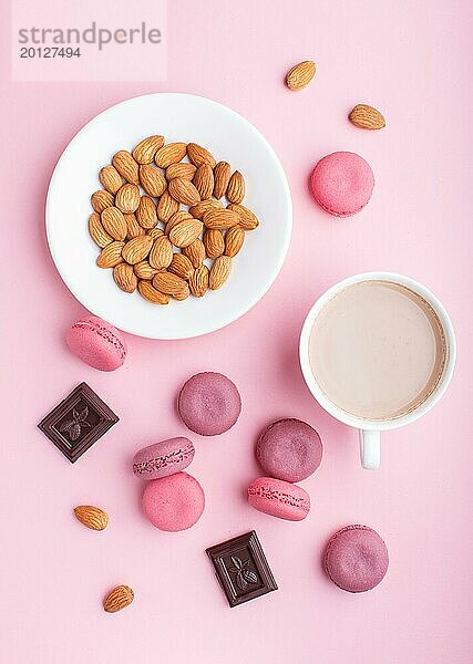 Lila und rosa Macaron oder Makronen Kuchen mit Tasse Kaffee und Mandeln auf Pastell rosa Hintergrund. Morninig  Frühling  Mode Zusammensetzung. Flachlage  Draufsicht  Muster