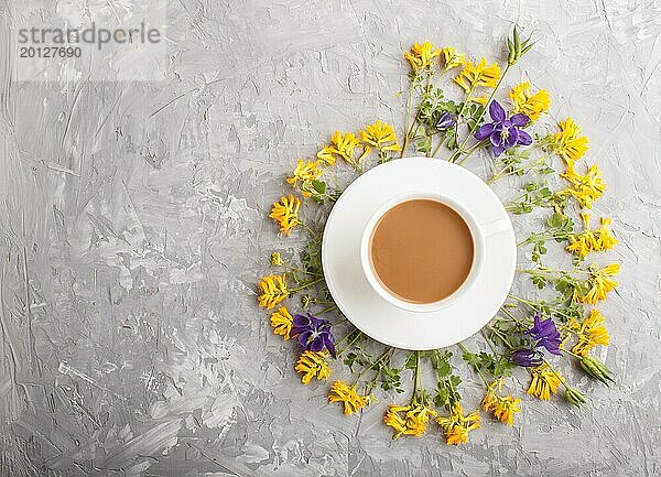 Gelbe und blaue Blumen in einer Spirale und eine Tasse Kaffee auf einem grauen Hintergrund aus Beton. Morninig  Frühling  Mode Zusammensetzung. Flachlage  Draufsicht  Kopierraum