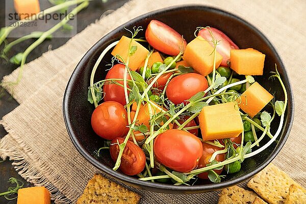 Vegetarischer Gemüsesalat aus Tomaten  Kürbis  mikrogrünen Erbsensprossen auf schwarzem Betonhintergrund und Leinentuch. Seitenansicht  Nahaufnahme  selektiver Fokus